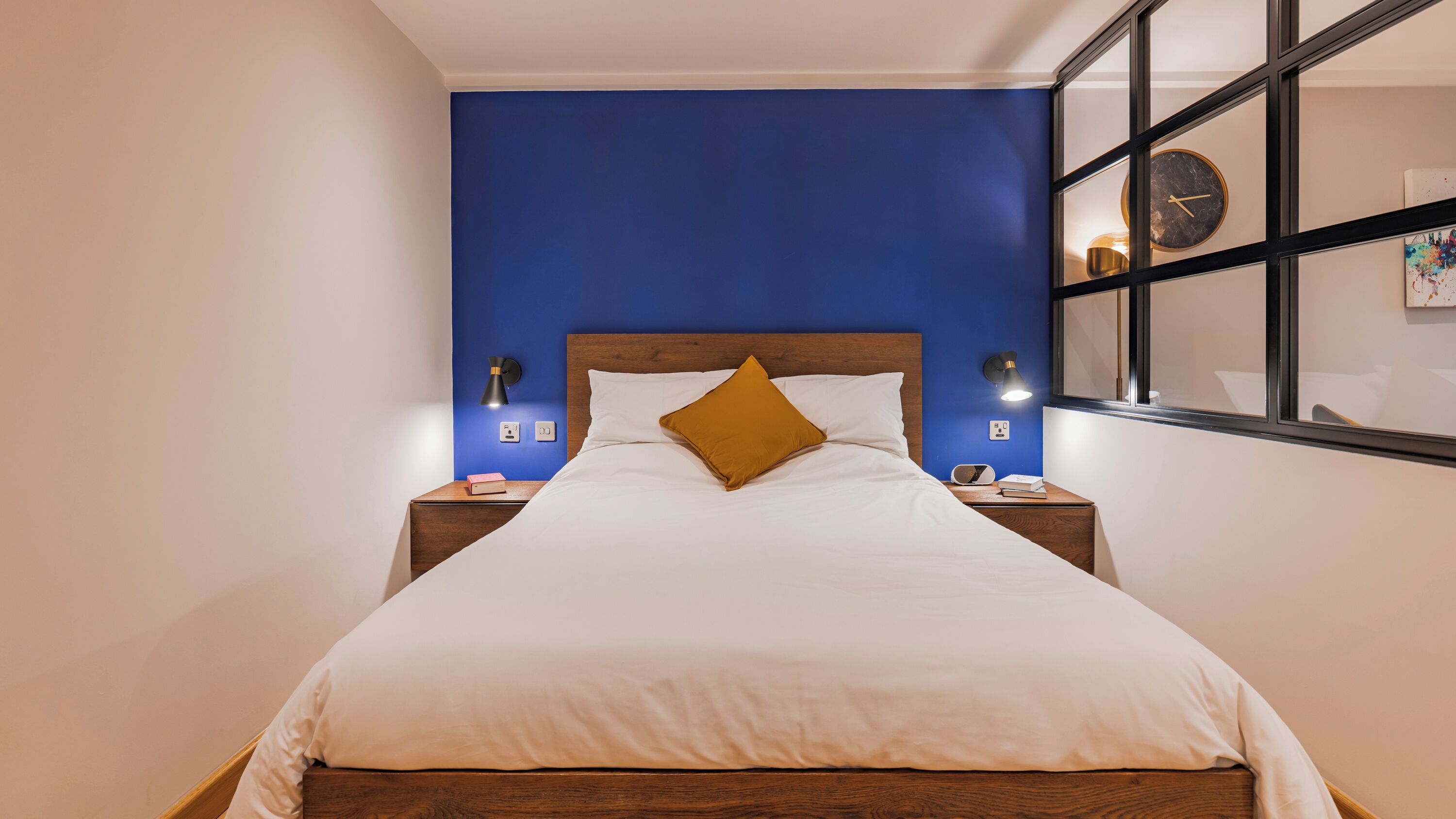 A bed with white bedding, a wooden headboard, and a single mustard-colored pillow.