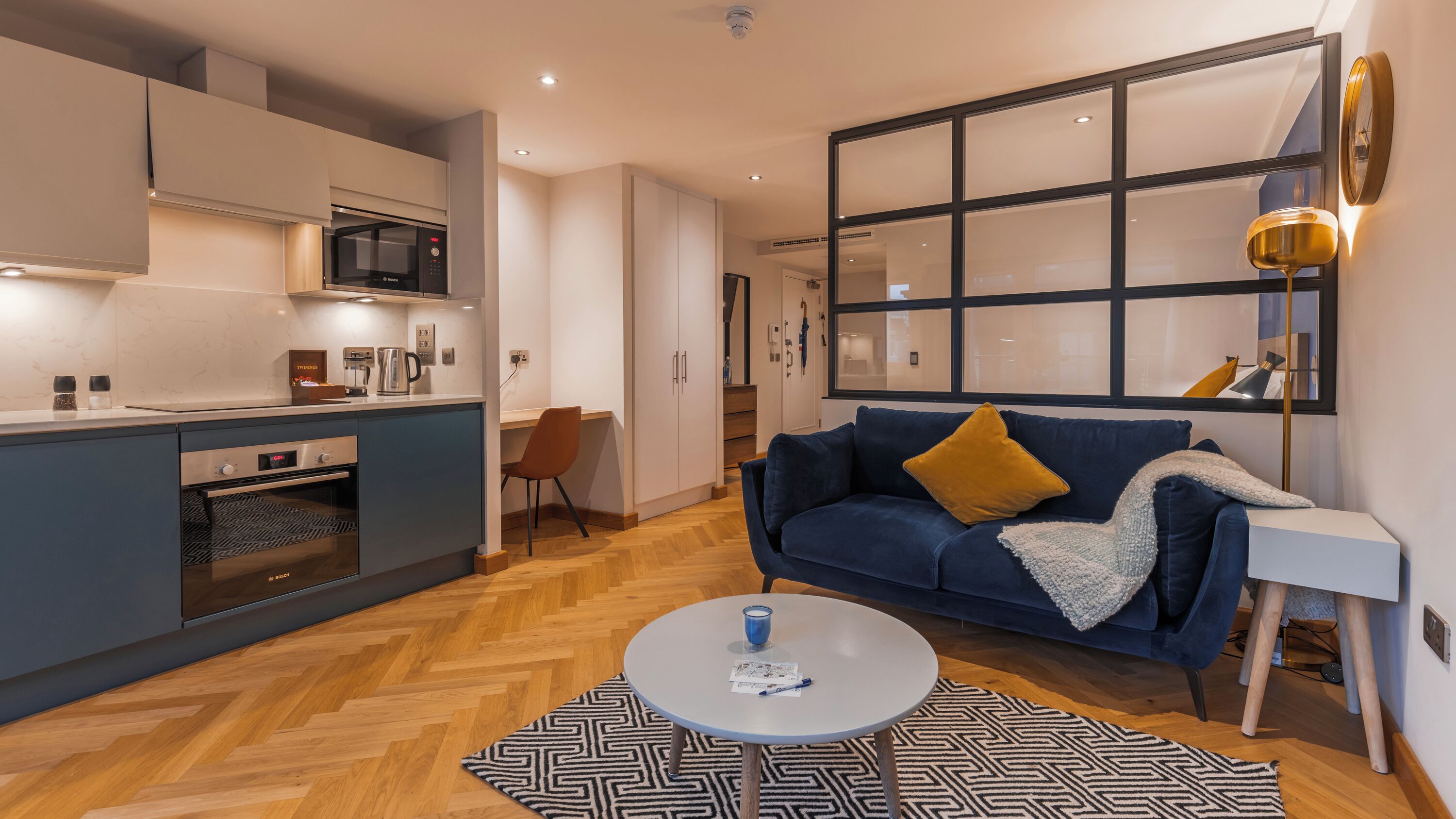 A modern apartment with a kitchen, a dining area, a living room with a sofa, and a large window.