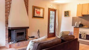 A living room with a fireplace, a sofa, and a kitchen area with cabinets. - Forest retreat, close to Barcelona and Beaches (Dosrius)