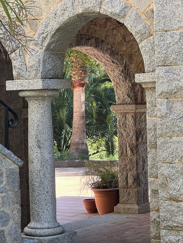 An arched stone structure with a palm tree and potted plants.
