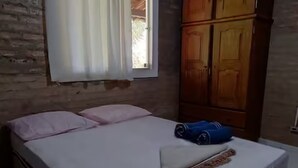 A room with a bed, a window with curtains, a wooden wardrobe, and a ceiling light.
