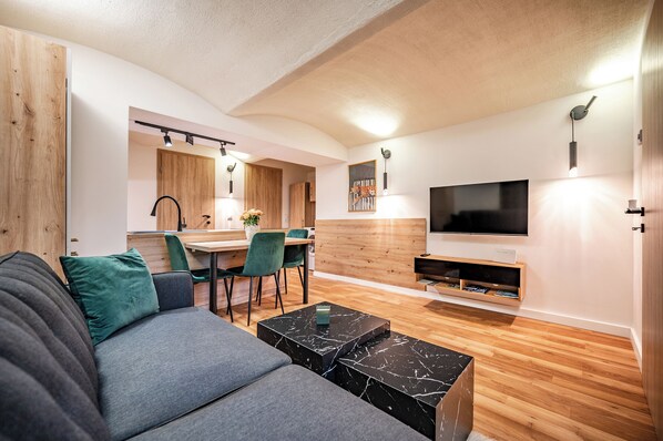 A modern living room with a sofa, a coffee table, a TV, and a dining area with chairs and a table.