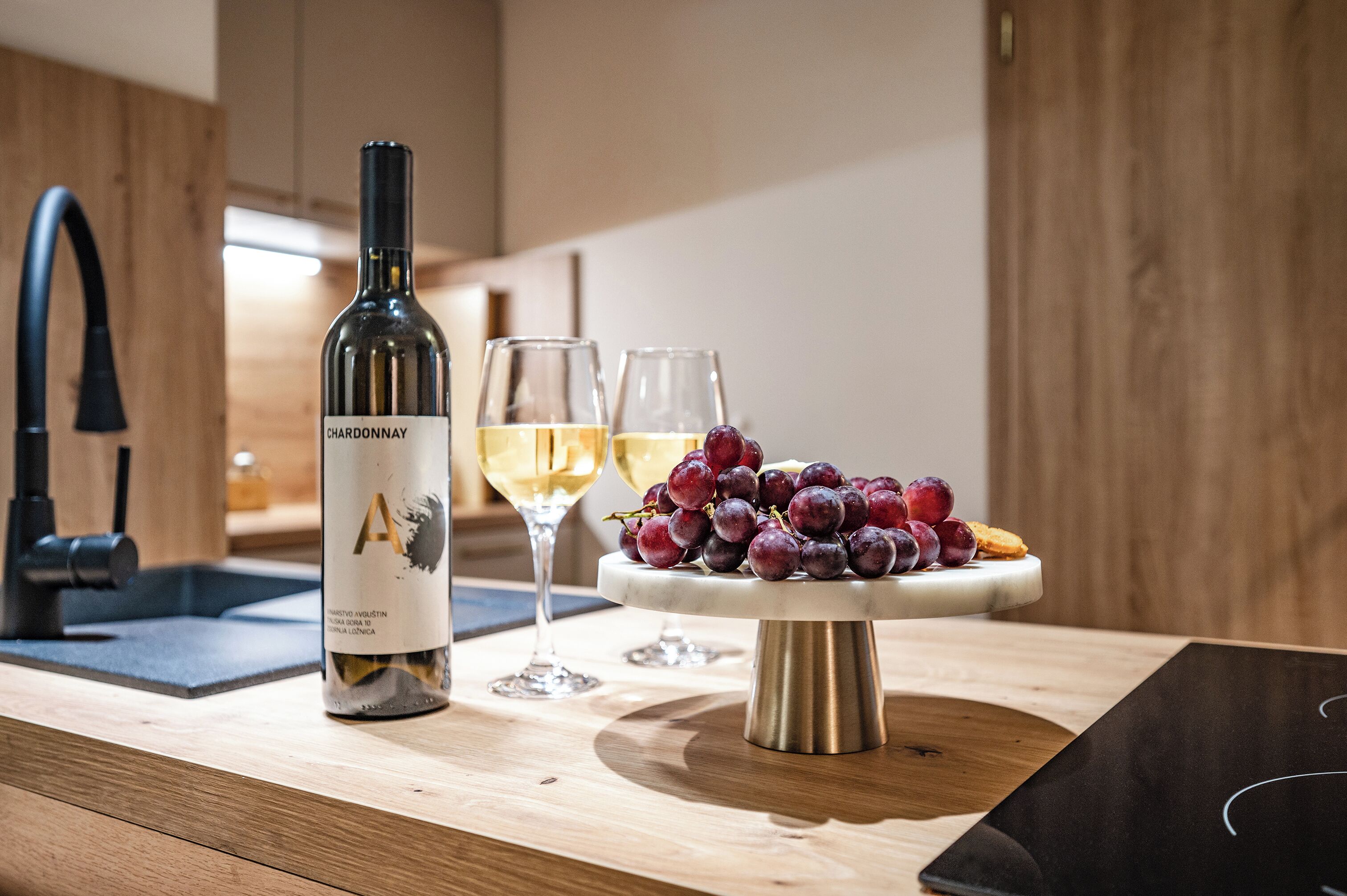 A kitchen counter with a wine bottle, glasses, and a fruit platter.