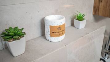 A spa candle labeled 'Nordic Sense' on a tiled surface with two potted plants.