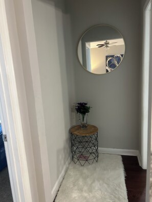 A hallway with a round mirror, a small wooden side table with a vase, and a white furry rug.
