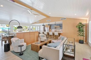 A modern living room with a sofa, armchairs, a coffee table, and a dining area with a kitchen in the background. - Pink Pearl Waterfront Retreat | Canal + Dock (Holmes Beach)