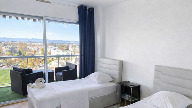A hotel room with two beds, a large window with a view, a small balcony, and a white rug. - Magnificent apartment in a private residence for 8 people, 5 minutes from Lyon, view of Part Dieu (Bron)