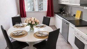 A compact kitchen with modern appliances, a dining area with a round table and chairs, and a view of buildings through a window. - Magnificent apartment in a private residence for 8 people, 5 minutes from Lyon, view of Part Dieu (Bron)