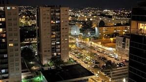 A nighttime cityscape with high-rise buildings, a parking area, and a street with illuminated buildings. - Magnificent apartment in a private residence for 8 people, 5 minutes from Lyon, view of Part Dieu (Bron)
