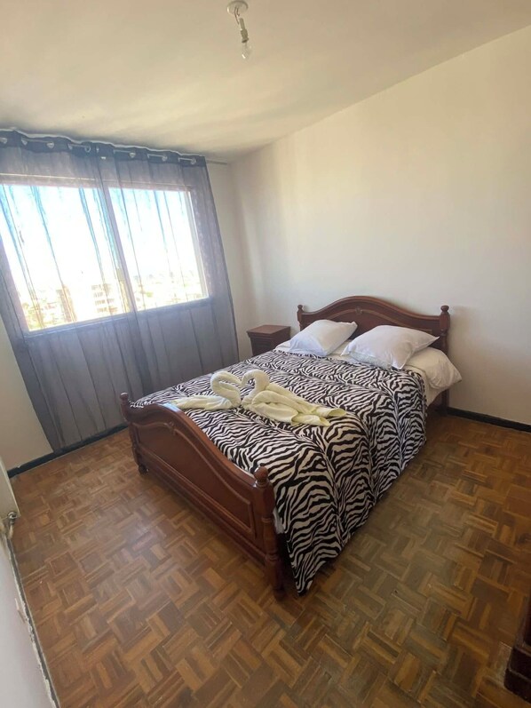 A bedroom with a zebra-patterned bedspread, a wooden headboard, a nightstand, and a window with curtains.