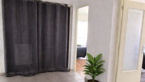 A room with a large window, a potted plant, and a door leading to another room. - Magnificent apartment in a private residence for 8 people, 5 minutes from Lyon, view of Part Dieu (Bron)