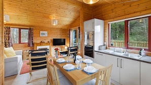 A wooden cabin interior with a dining area, kitchen, and a TV.