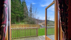 A wooden deck with a glass door leading to a view of a forested hillside.