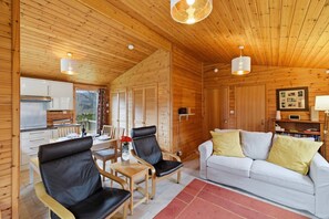 A wooden cabin interior with a dining area, a sofa, and a kitchen.