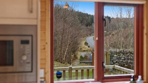 A room with a view of a forested area, a stone wall, and a wooden deck.