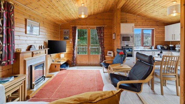 A wooden cabin interior with a living room, dining area, kitchen, and a fireplace.