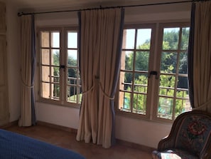 Ein Zimmer mit großen Fenstern, einem Bett und einem Sessel.