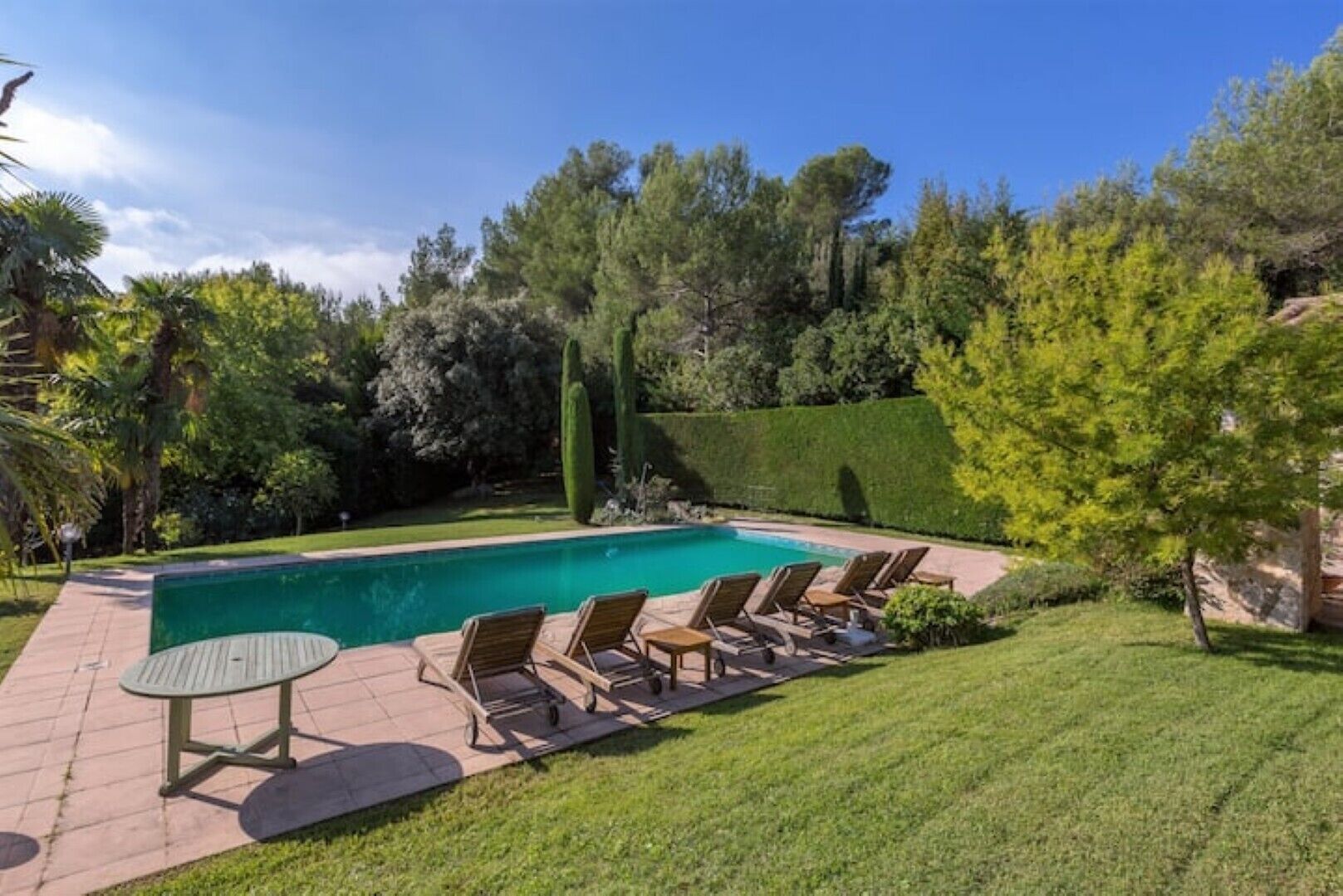A swimming pool with lounge chairs, a table, and a well-maintained lawn.