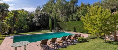 A swimming pool with lounge chairs, a table, and a well-maintained lawn.