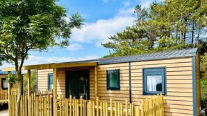 A wooden mobile home with a fenced outdoor area, windows, and a clear sky. - Camping Cristal d'Opale (Dannes)