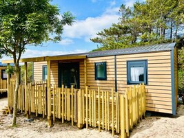 A wooden mobile home with a fenced outdoor area, windows, and a clear sky.