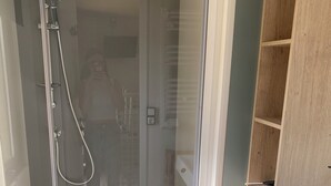 A modern bathroom with a glass-enclosed shower, a wooden vanity, and a built-in shelving unit. - Camping Cristal d'Opale (Dannes)