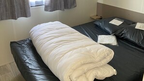 A bed with a white duvet, a black mattress, and a wooden headboard. - Camping Cristal d'Opale (Dannes)