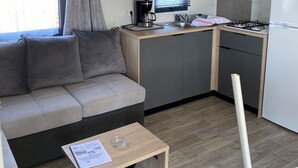 A compact kitchenette with a microwave, coffee maker, and gas stove. There's a sofa and a small table with a glass and a booklet. - Camping Cristal d'Opale (Dannes)
