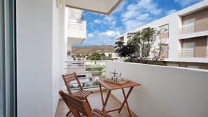 A balcony with a table and chairs, a potted plant, and a view of a mountain. - Cozy Stay in Modern Apt / Clean Comfortable & Calm (Imi Ouaddar)