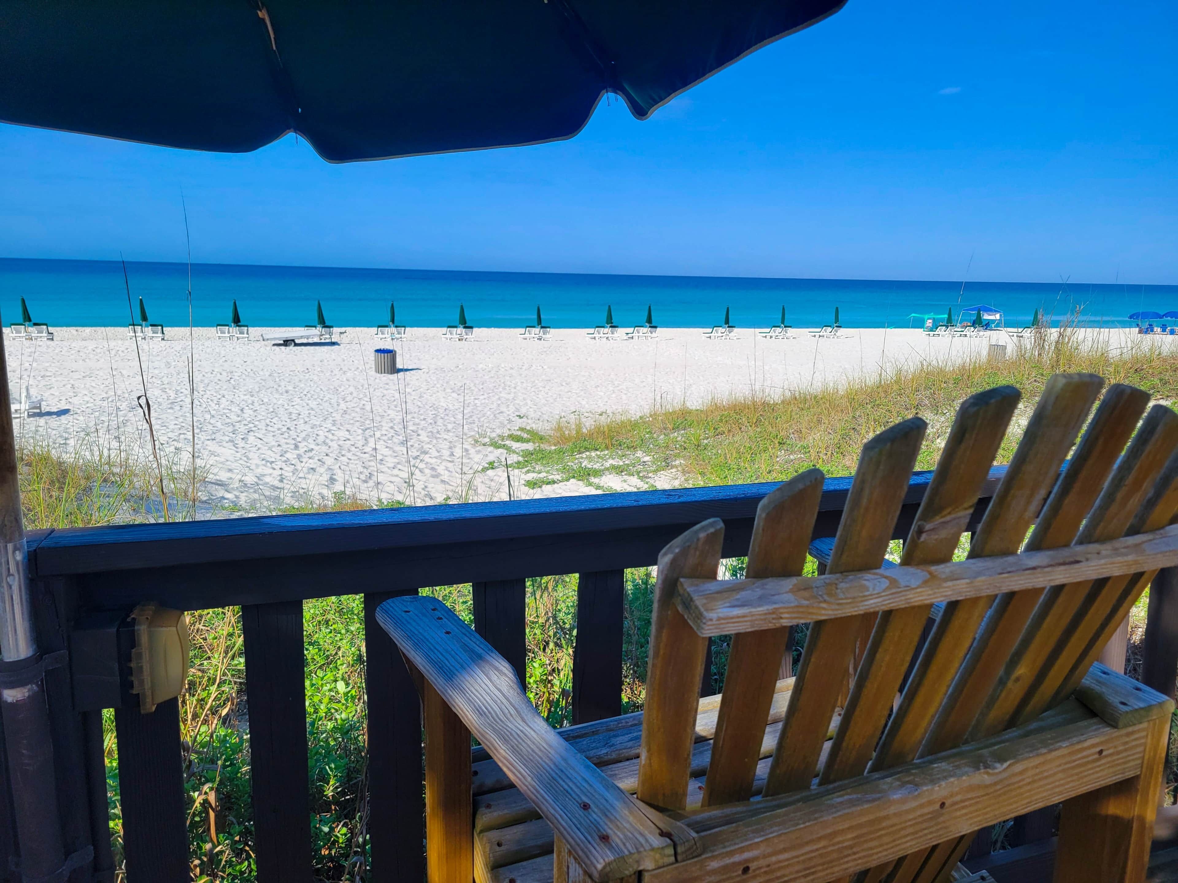 Una silla de madera con vista a una playa y una vista despejada del océano y sombrillas.