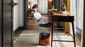 A room with a modern chair, a table, a hanging light fixture, and a view through an archway to another room.