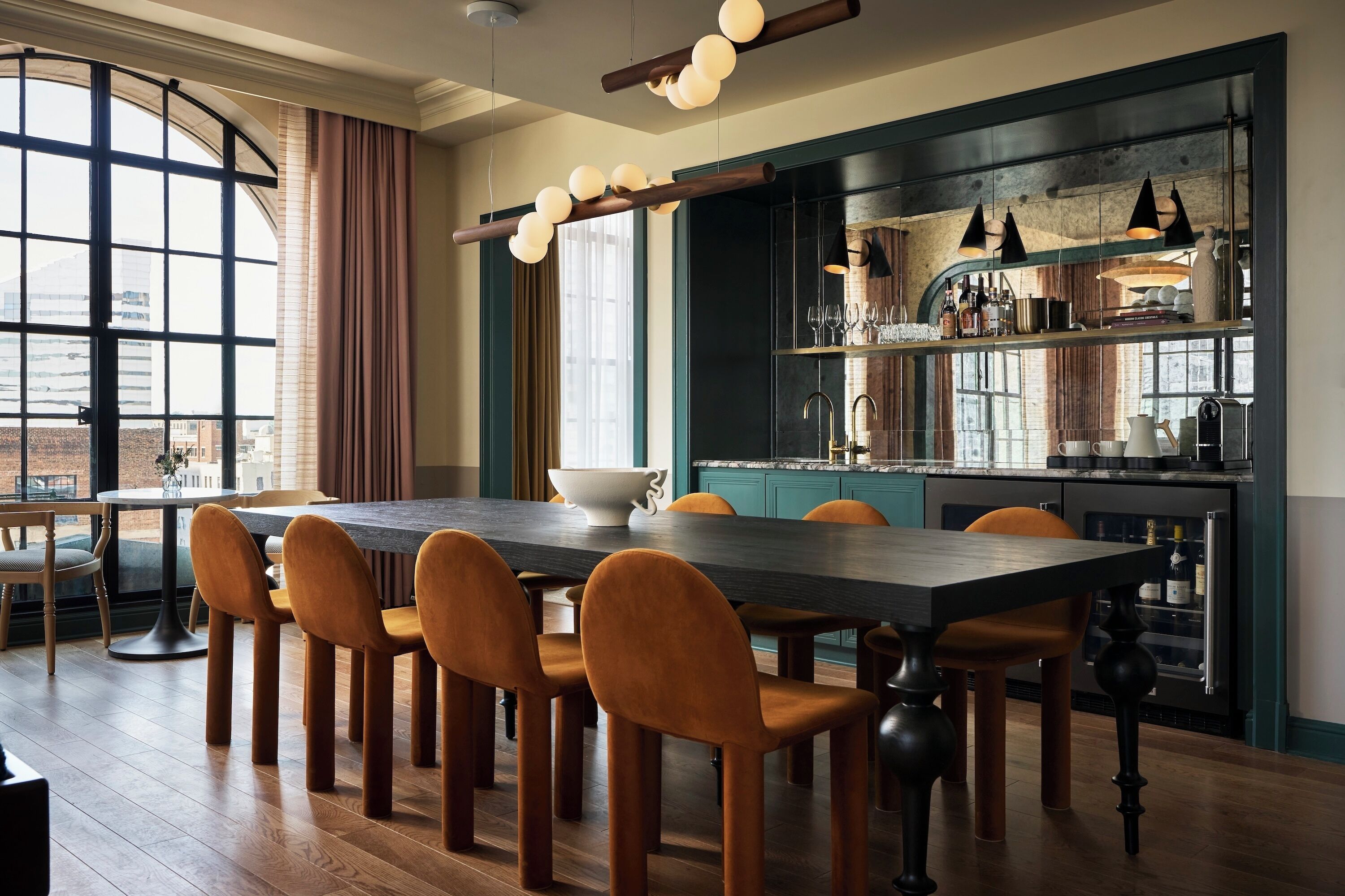 A dining area with a long table, chairs, and a kitchen in the background.