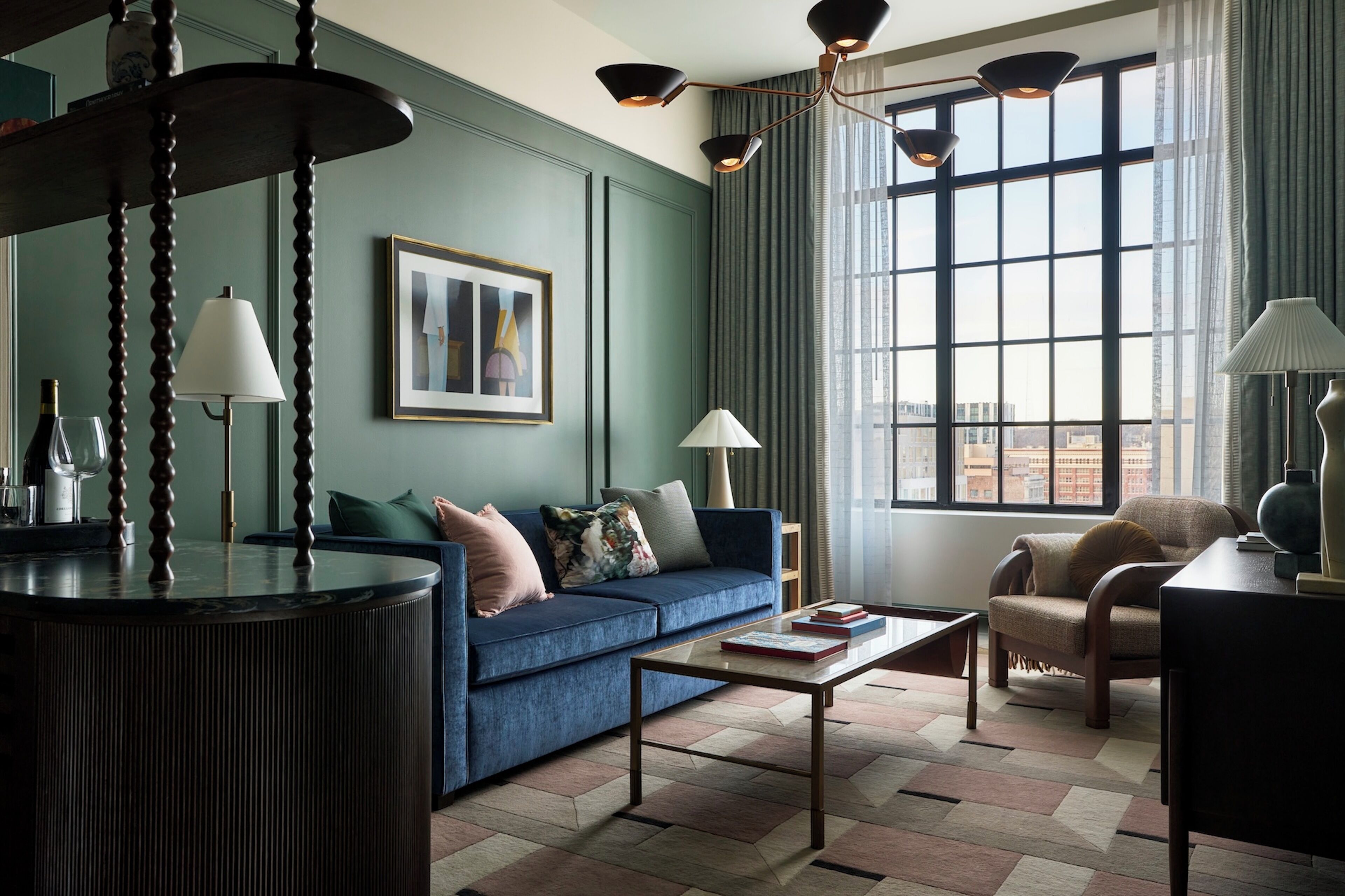 Una sala de estar moderna con un sofá azul, una mesa de centro y vistas de un paisaje urbano a través de amplios ventanales.