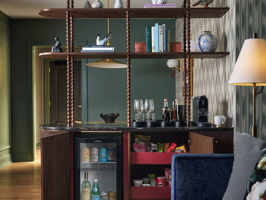 Una sala de estar moderna con un sofá azul oscuro, una mesa de centro, una estantería y un refrigerador pequeño.