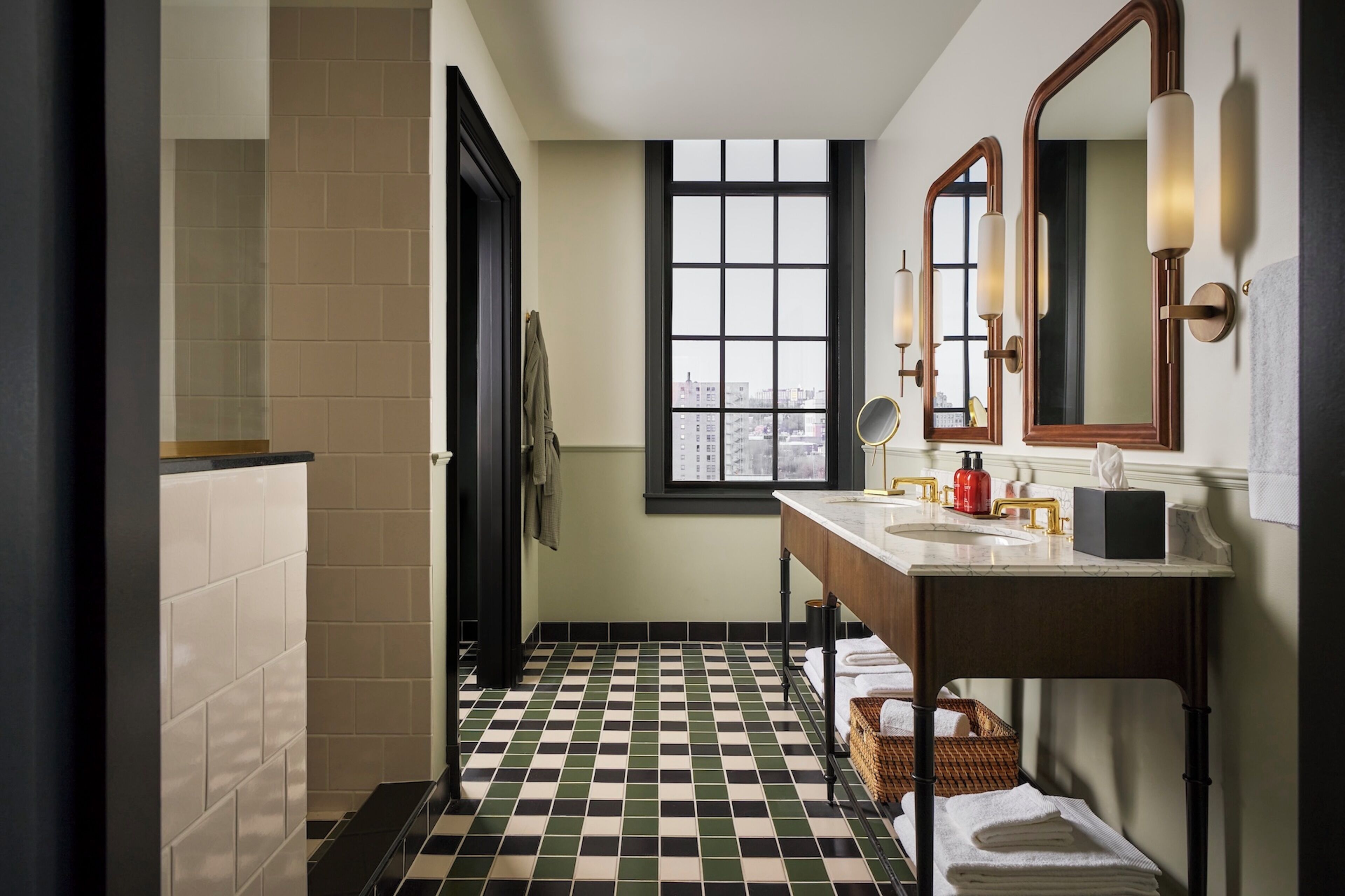 A bathroom with a checkered floor, a window with a city view, a sink with a mirror, and a towel rack.
