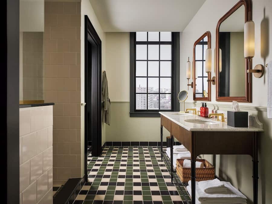 A bathroom with a checkered floor, a window with a city view, a sink with a mirror, and a towel rack.