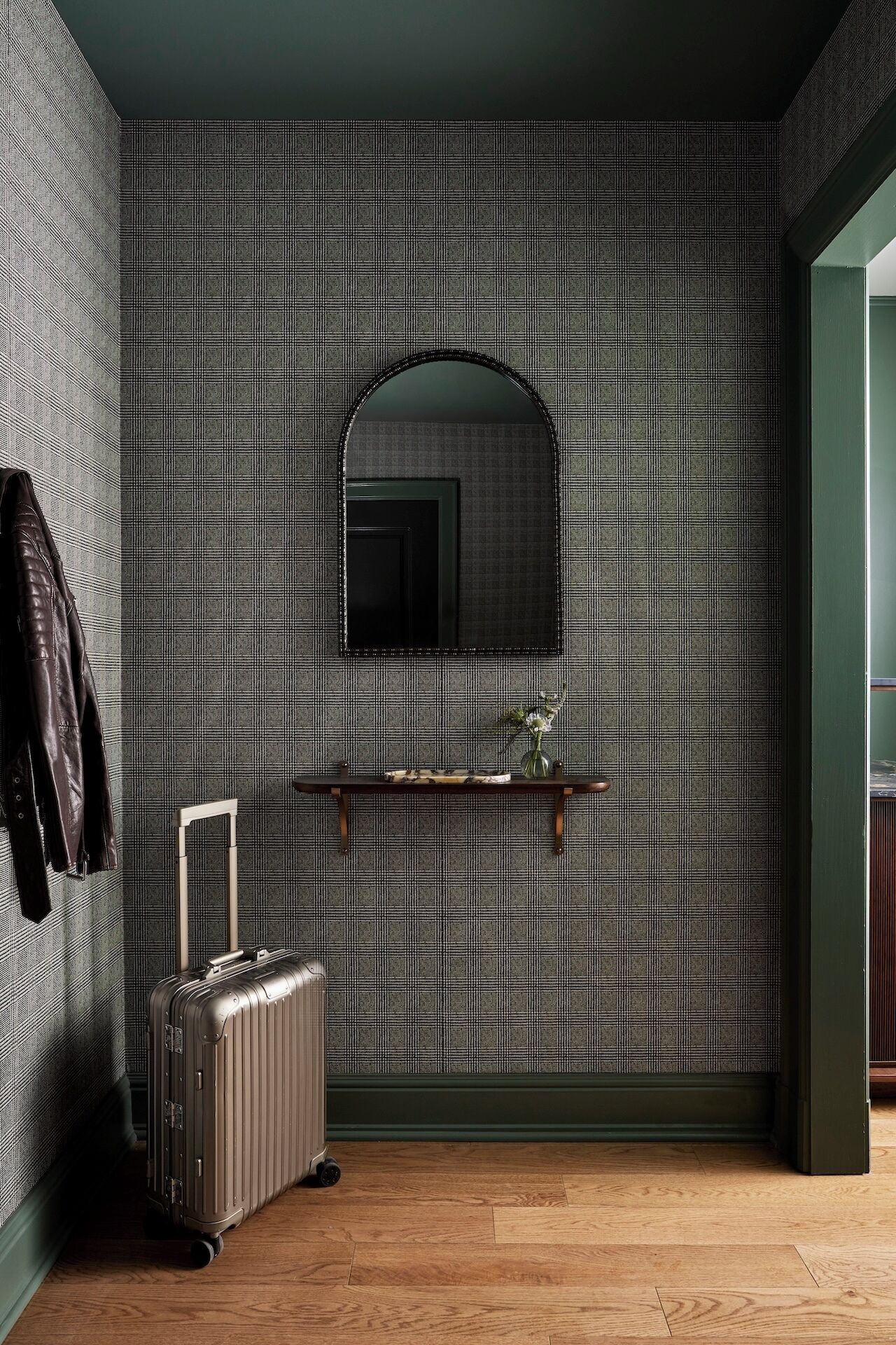 A room with a patterned wallpaper, a mirror, a wooden floor, and a suitcase.
