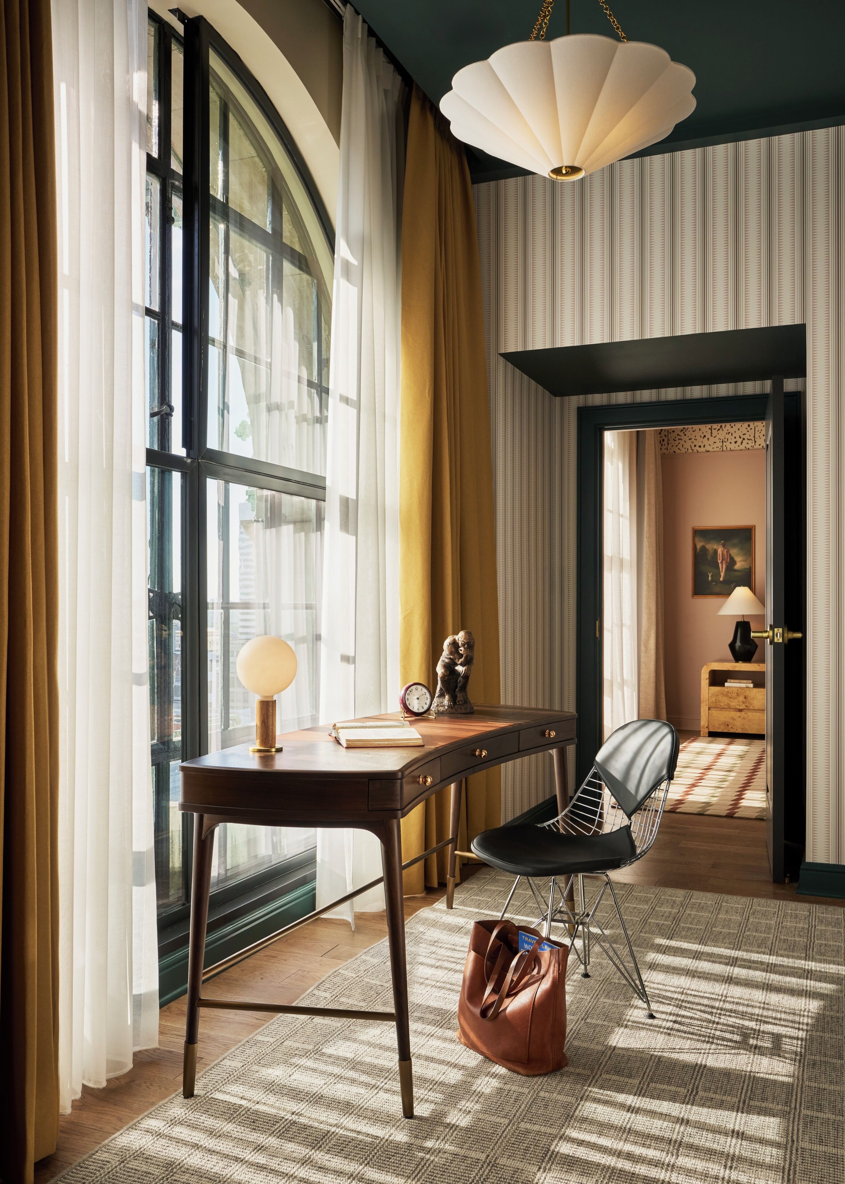 A room with a desk, chair, lamp, and a view through a window.