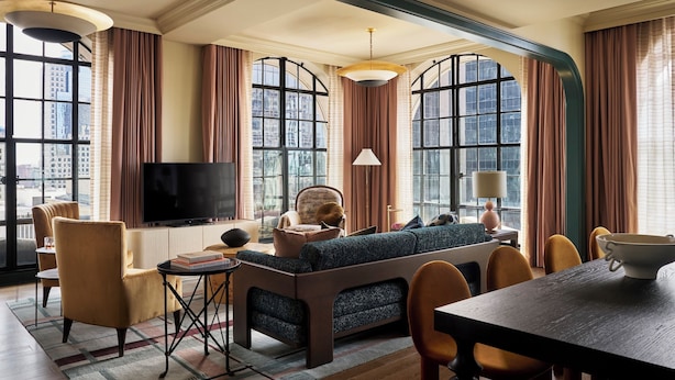 A modern living room with a sofa, chairs, a TV, and large windows with curtains.