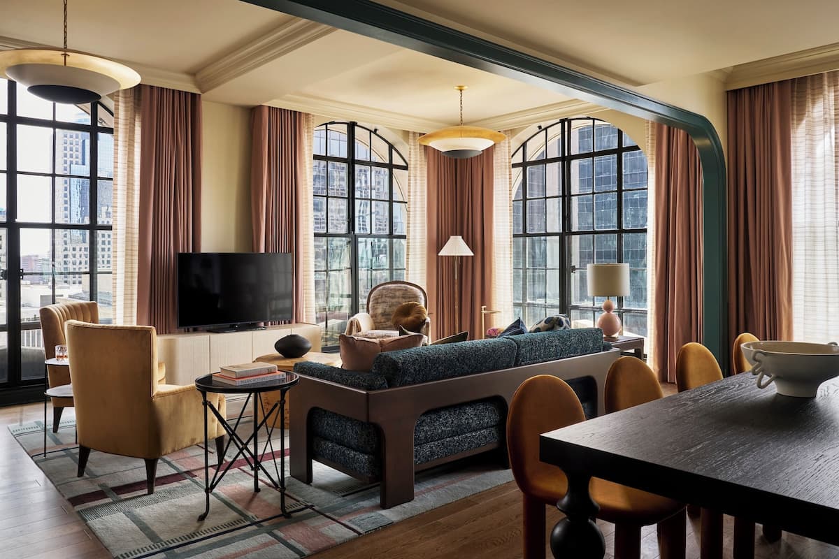 A modern living room with a sofa, chairs, a TV, and large windows with curtains.
