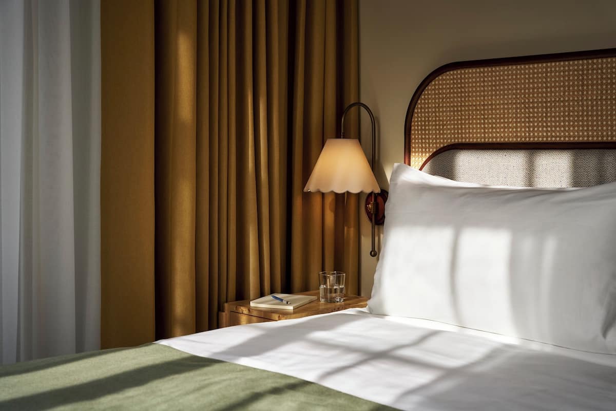 A neatly made bed with a pillow, a bedside table with a lamp, a glass of water, and a book.