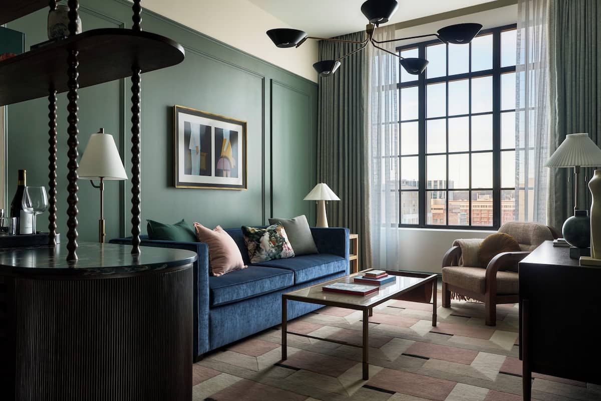 A modern living room with a blue sofa, a coffee table, and a view of the city through large windows.