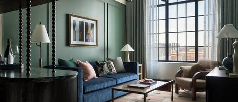 A modern living room with a blue sofa, a coffee table, and a view of the city through large windows.