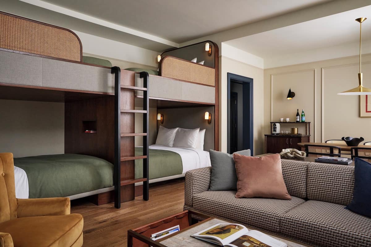 A hotel room with bunk beds, a sofa, a coffee table, and a desk with a lamp.