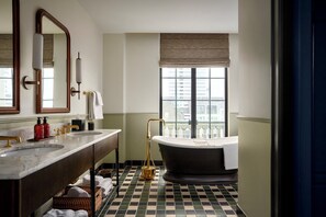 Un baño con una bañera grande, dos lavamanos, un espejo y una ventana con vistas a edificios.