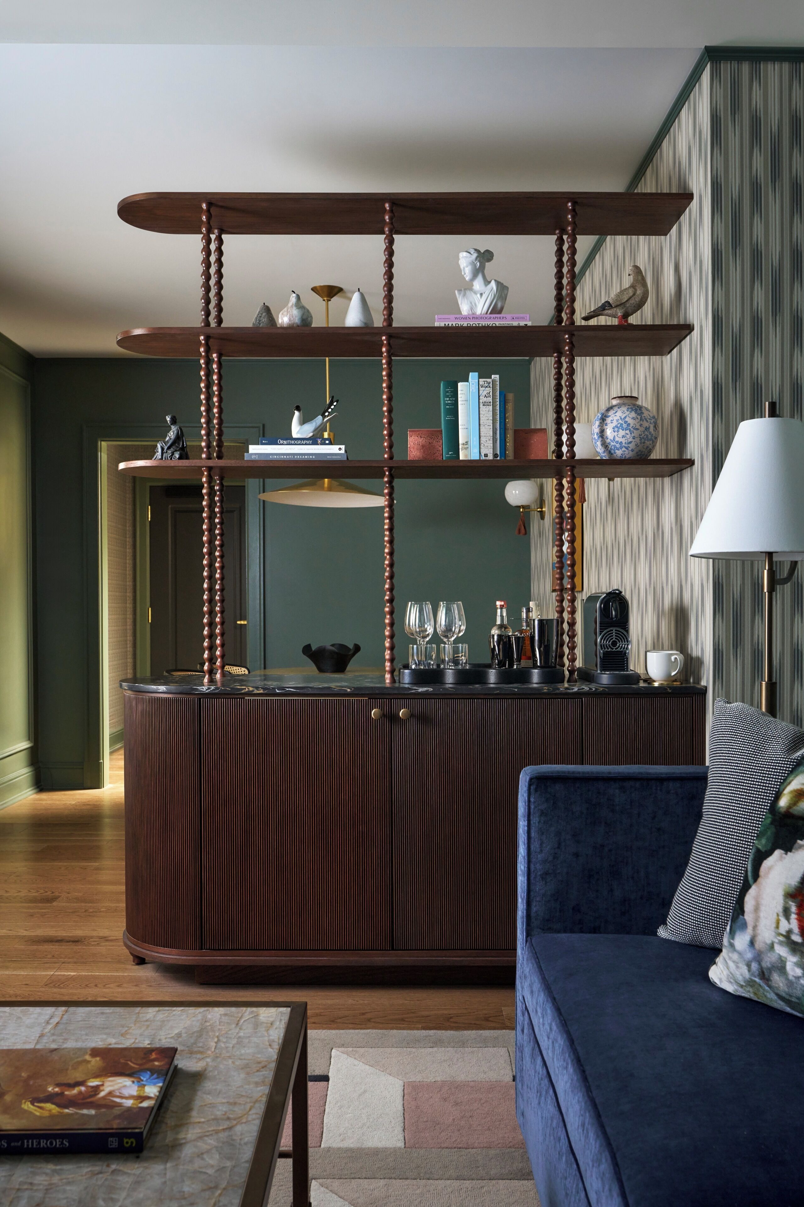 A modern living room with a wooden coffee table, a blue sofa, and a bookshelf with decorative items.