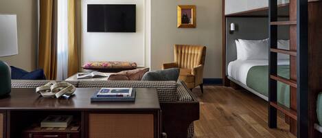 A hotel room with a bunk bed, a desk with a lamp, a chair, a television, and a framed picture on the wall.