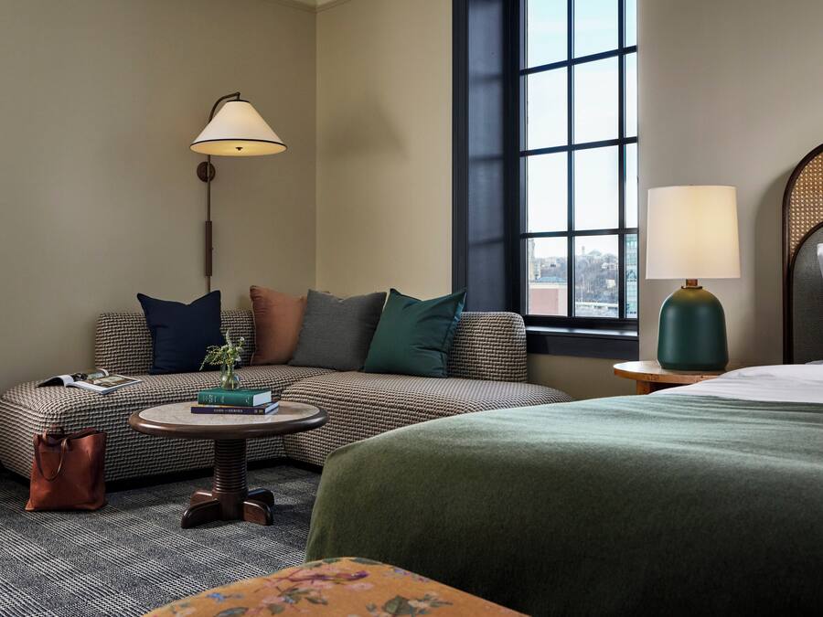Een hotelkamer met een bank, een ronde tafel, een lamp, een bed en een raam met uitzicht.