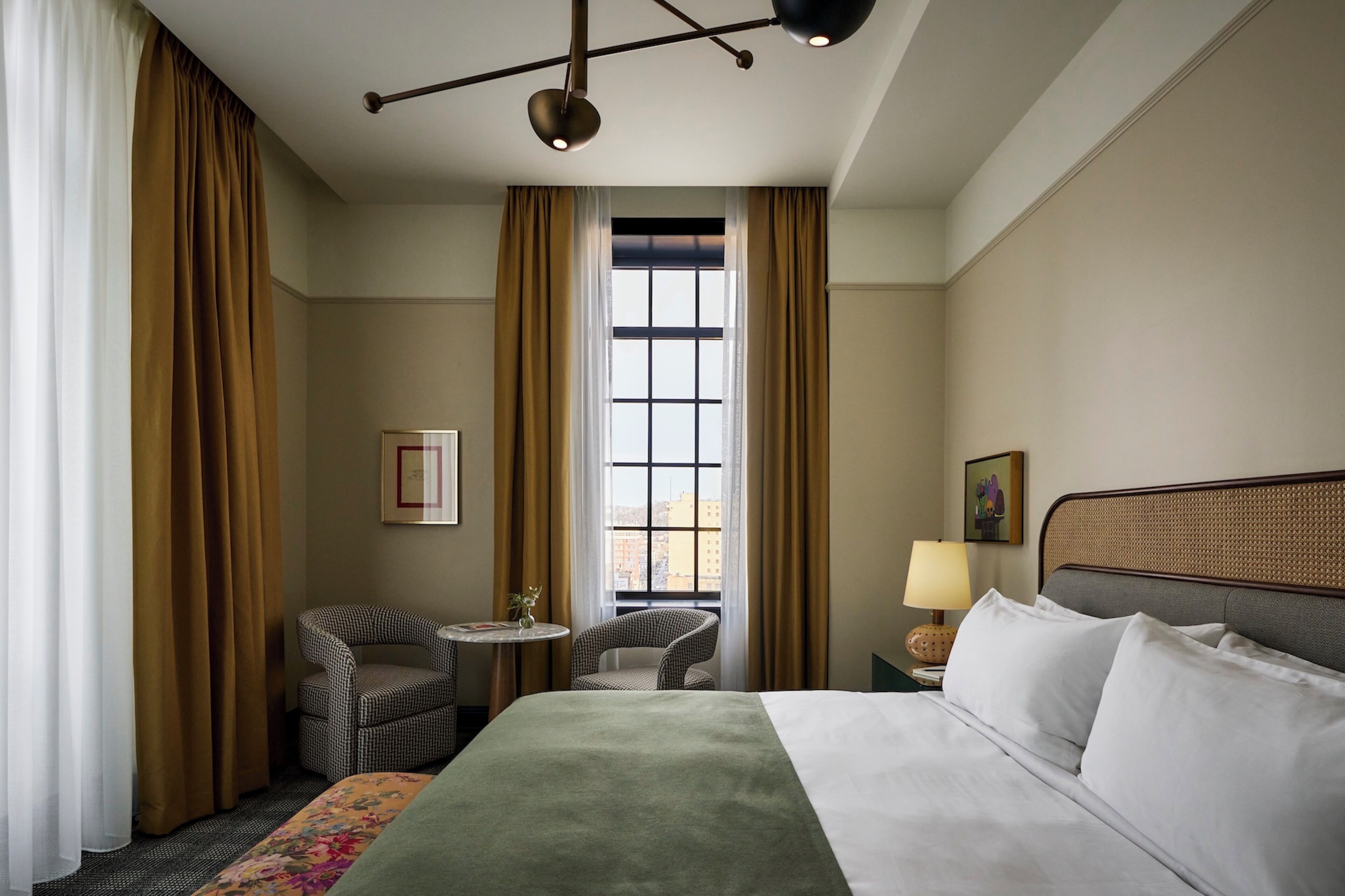 A hotel room with a bed, two chairs, a small table, a lamp, and a window with curtains.
