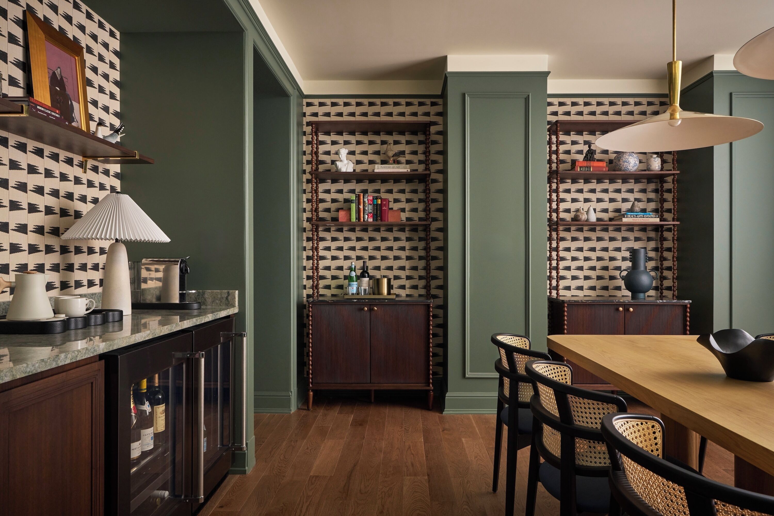 Un comedor con una mesa y sillas de madera, una estantería y una zona de cocina con encimera y armarios.